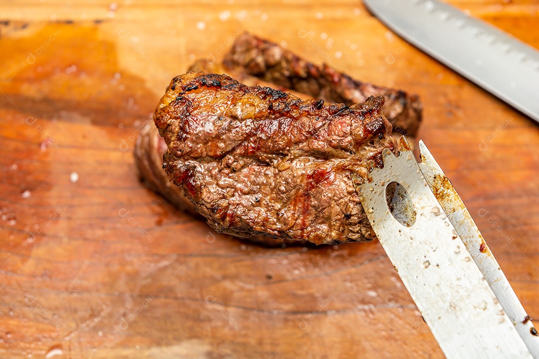 Pinça de churrasco segurando bife grelhado