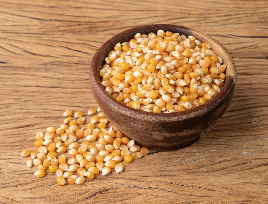 Grãos de milho ou pipoca secos em uma tigela sobre a mesa de madeira.