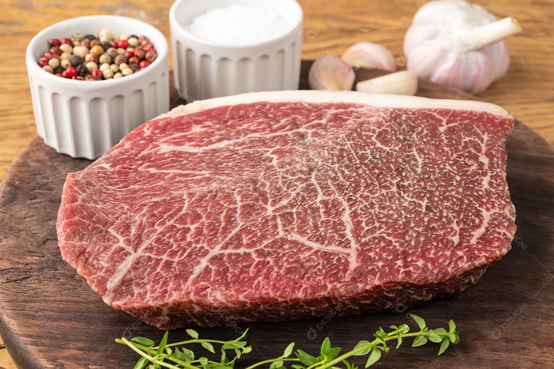 Carne assada de ombro wagyu crua sobre tábua de madeira com temperos.