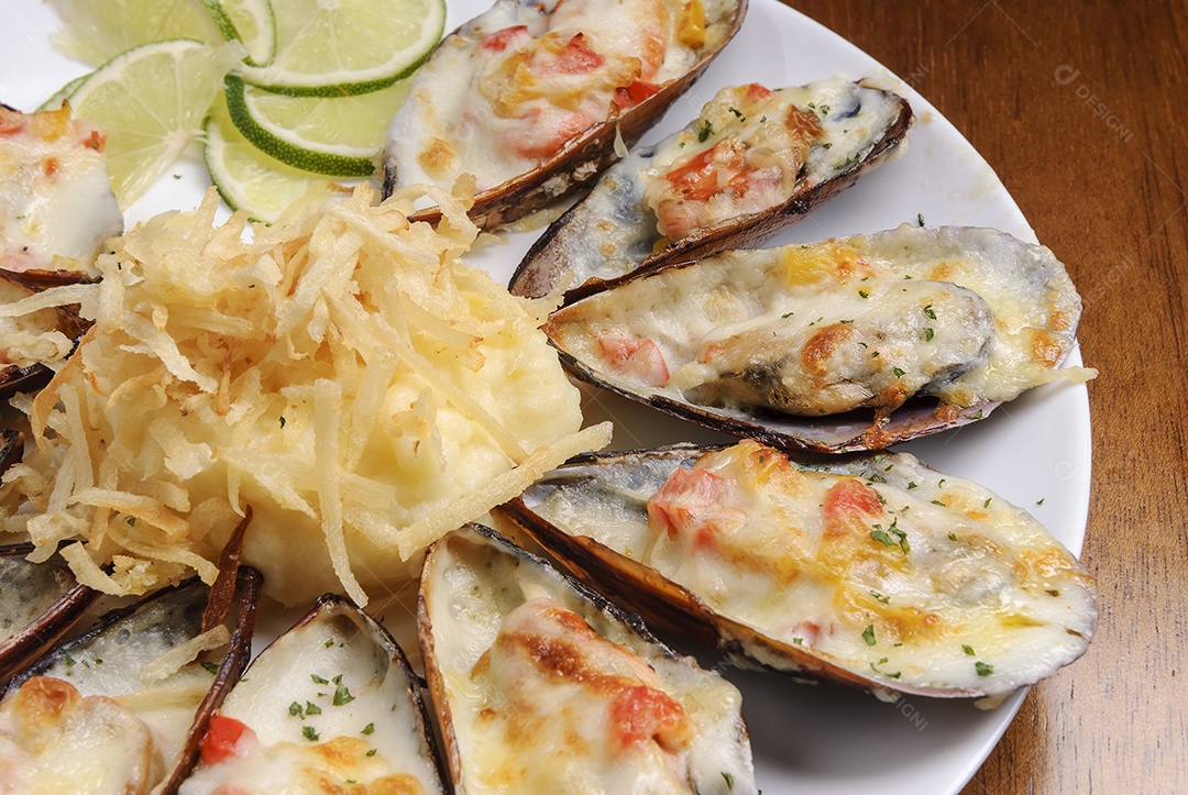 Mexilhões assados ​​gratinados com purê de batatas em um prato branco na mesa de madeira. frutos do mar brasileiros.