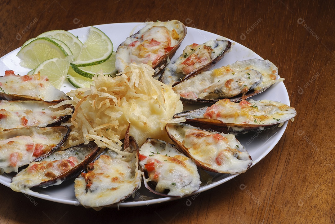 Mexilhões assados ​​gratinados com purê de batatas em um prato branco na mesa de madeira. frutos do mar brasileiros.