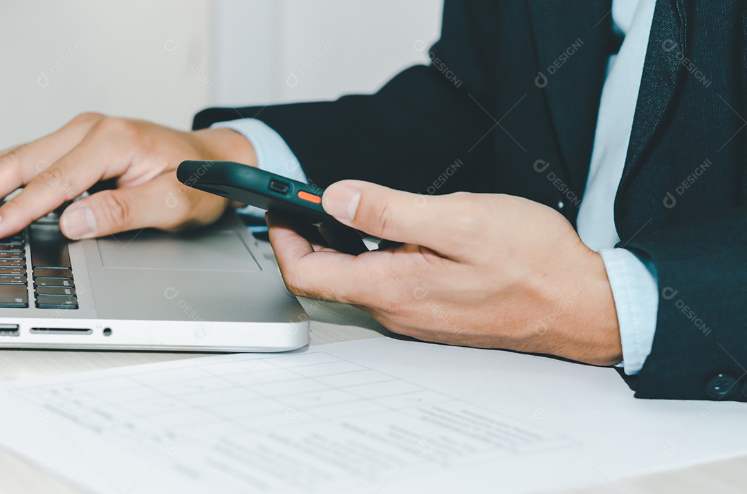 Empresário segurando telefone inteligente e computador portátil.