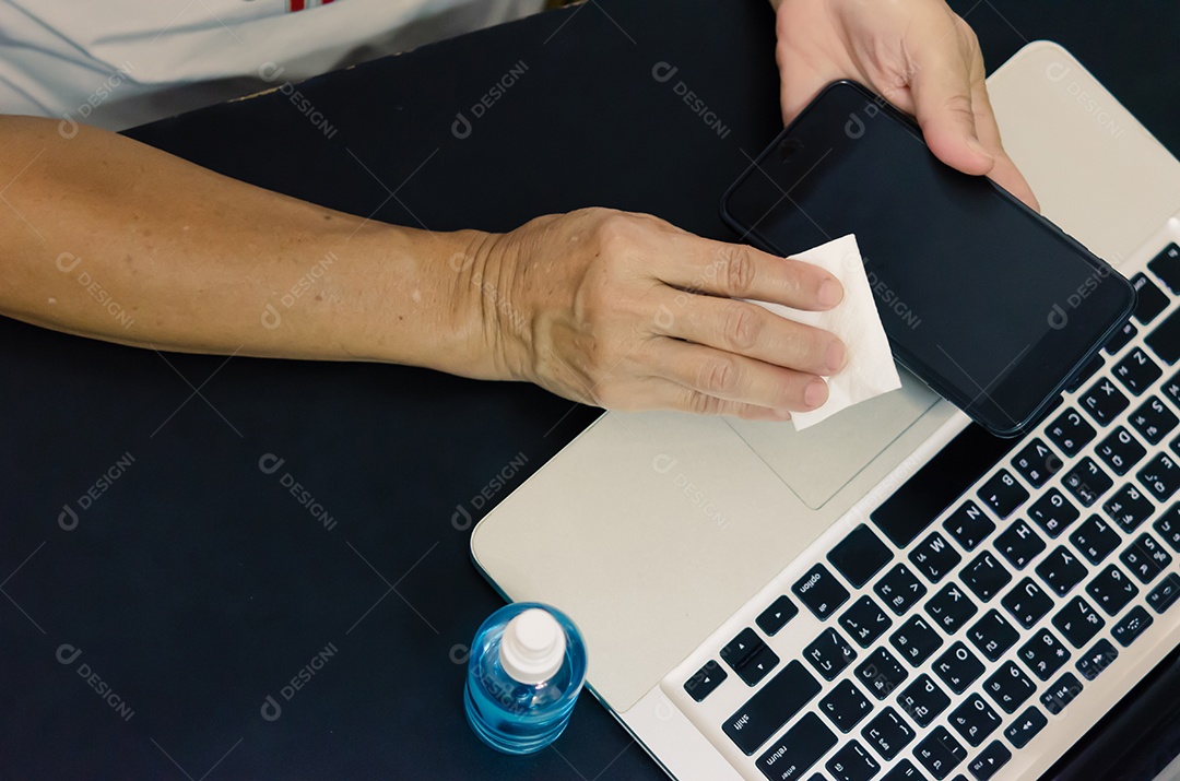 Mulher limpando e desinfetando seu notebook e celular com álcool. Conceito de cuidados de saúde para prevenir doenças