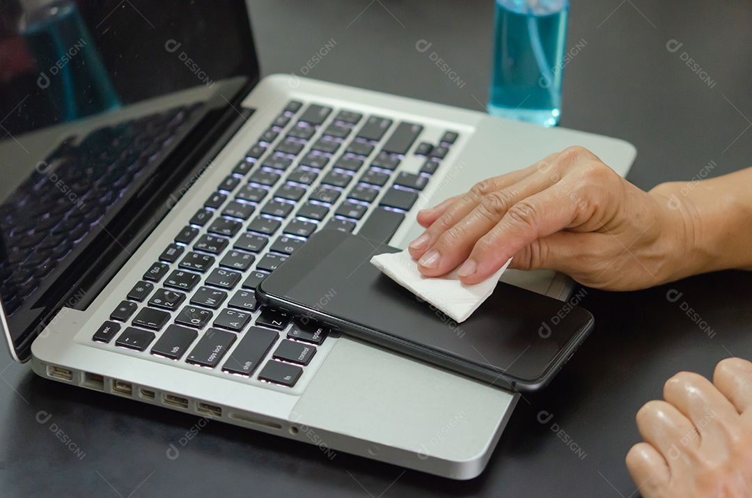 Woman cleaning and disinfecting her notebook and cell phone with alcohol. Health care concept to prevent disease