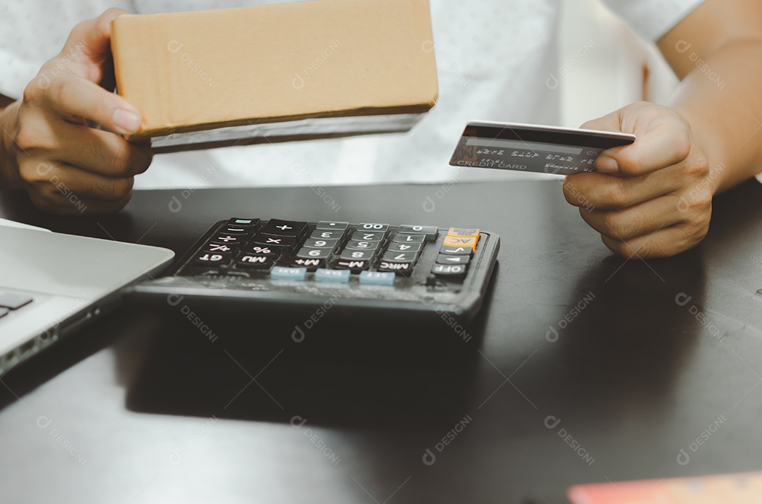 Mão de homem segurando o cartão de crédito e a caixa de encomendas. Conceito de negócio de compras online.