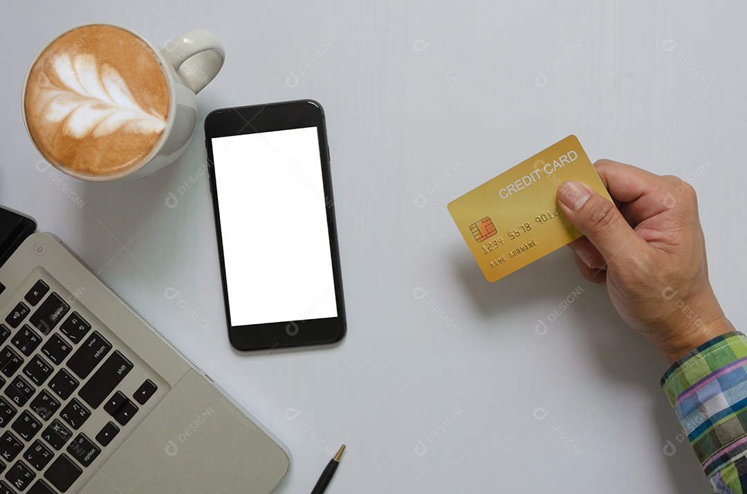 Vista superior de um homem segurando um cartão de crédito celular simulado tela branca em branco e computador e café Tecnologia de comunicação empresarial, conceito de compras on-line.