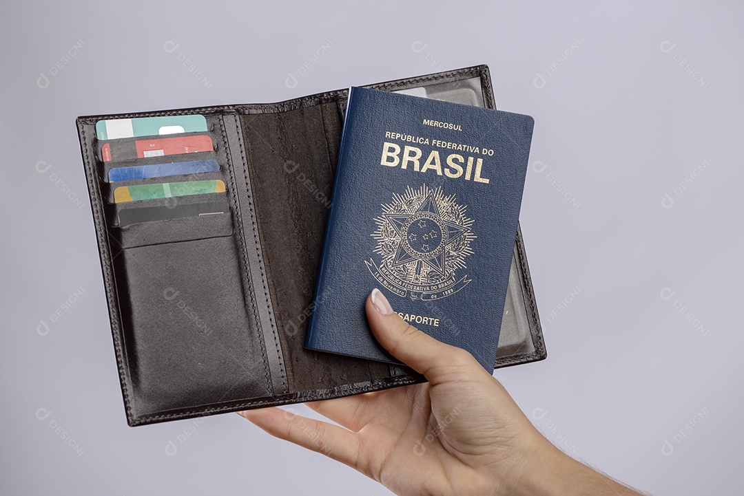 Passaporte brasileiro em uma mão com carteira, cartões de crédito e notas de euro em um fundo branco.