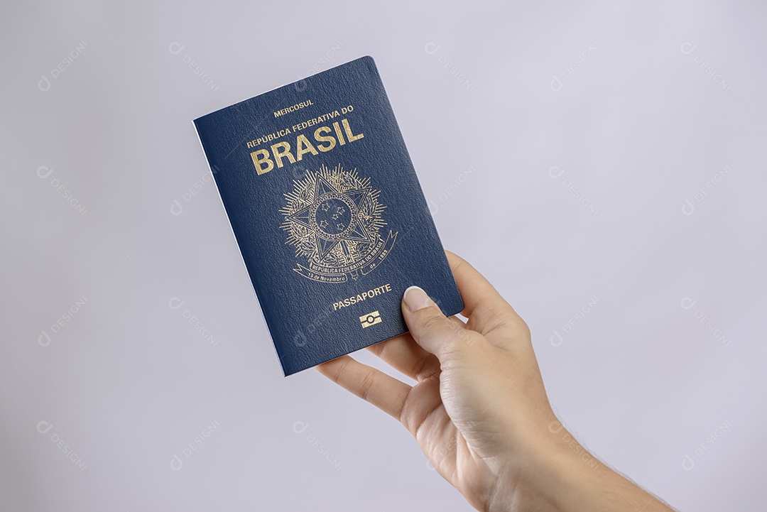Passaporte brasileiro em uma mão com fundo branco.