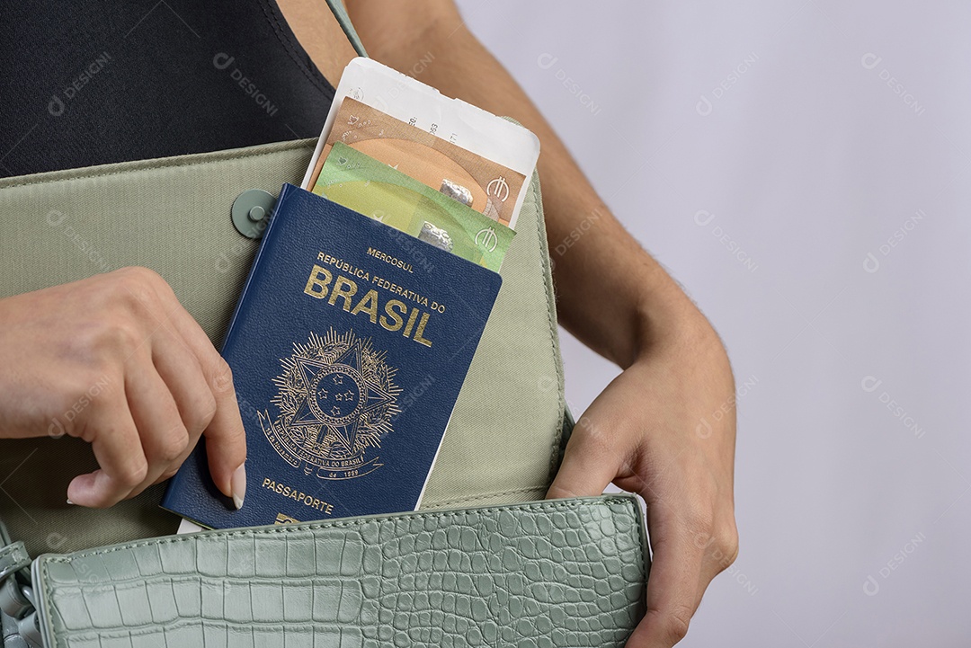 Passaporte brasileiro. Mãos colocando passaporte brasileiro na bolsa feminina verde.
