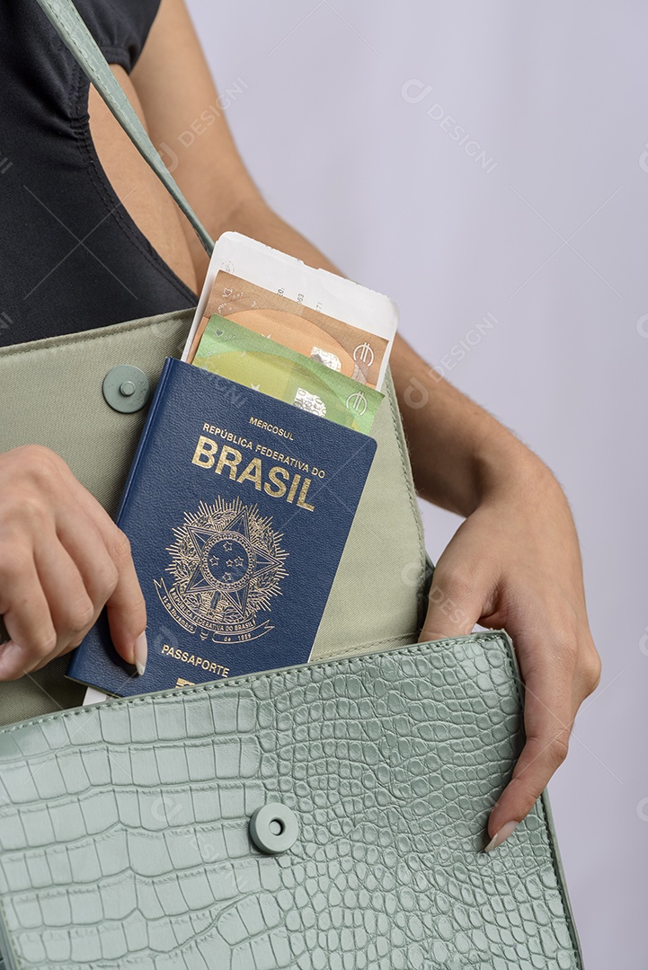 Passaporte brasileiro. Mãos colocando passaporte brasileiro na bolsa feminina verde.