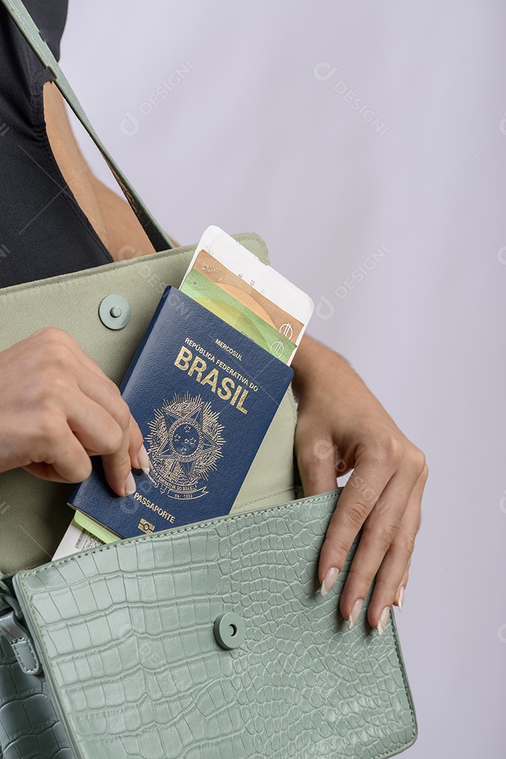 Passaporte brasileiro. Mãos colocando passaporte brasileiro na bolsa feminina verde.