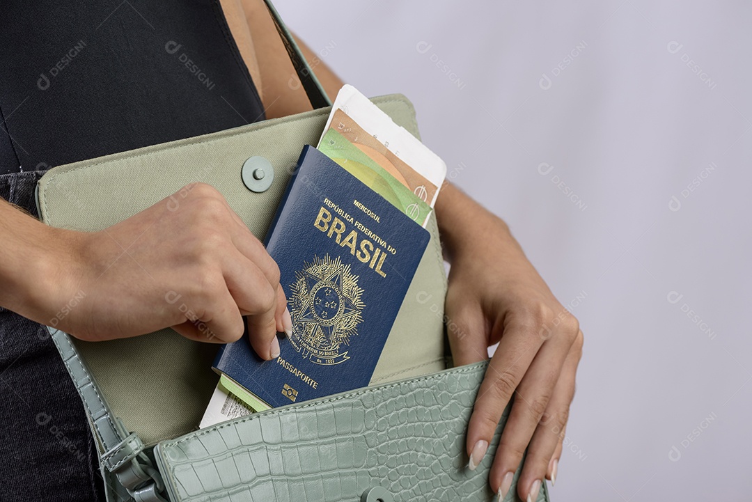 Passaporte brasileiro. Mãos colocando passaporte brasileiro na bolsa feminina verde.