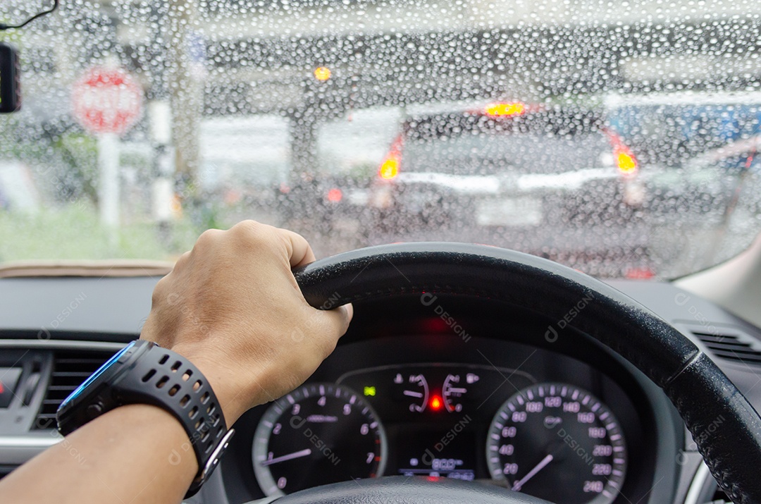 Hand driving blurred rain traffic jam background.