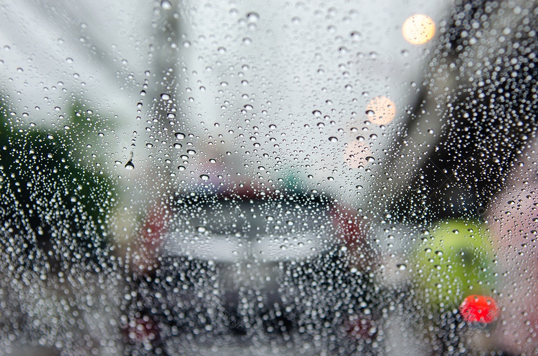Janela do carro com gotas de chuva dirigindo na chuva fundo de engarrafamento desfocado