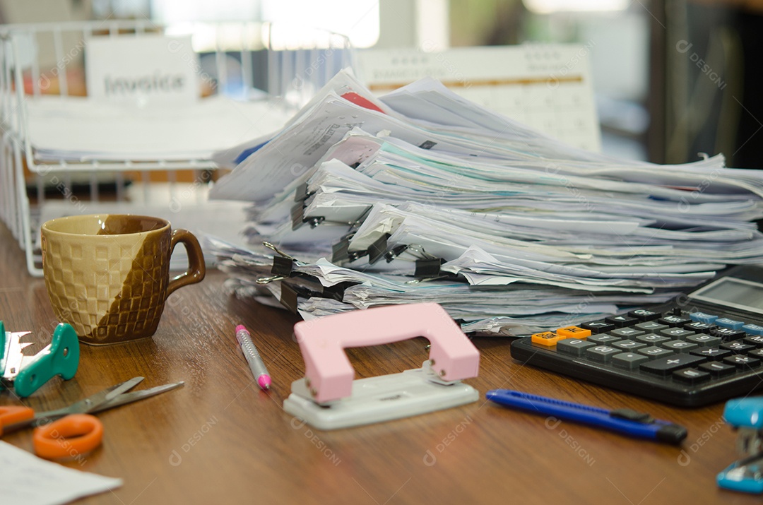 Pilha de papéis e equipamentos de escritório na mesa.