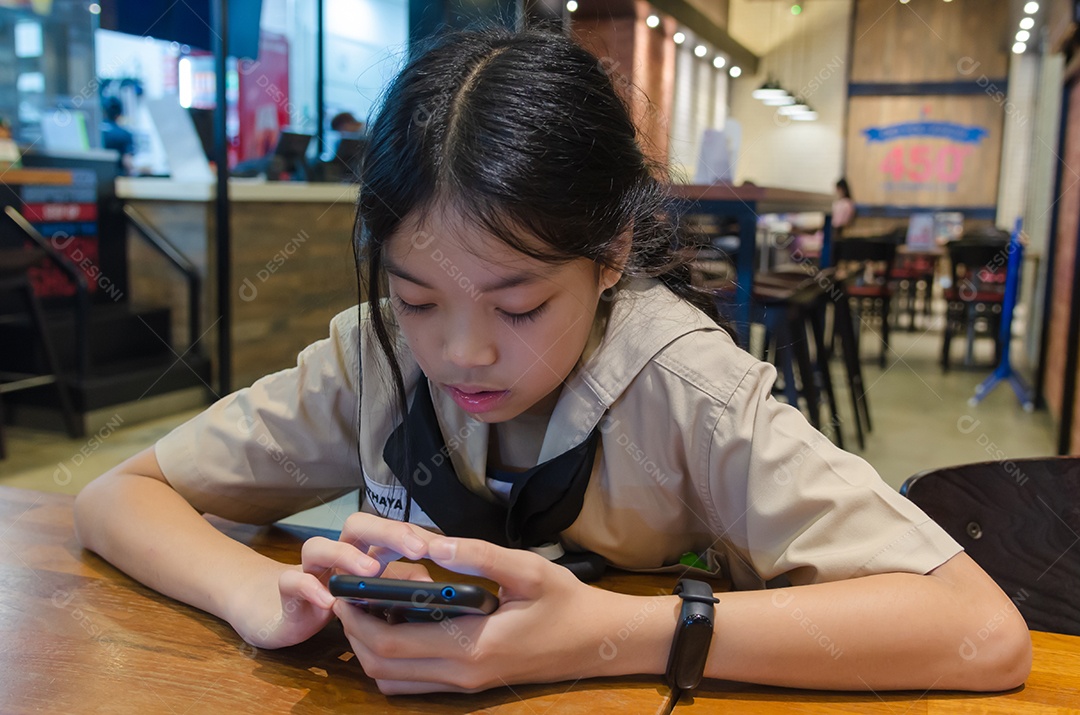 Crianças asiáticas jogando celular na mesa de jantar.