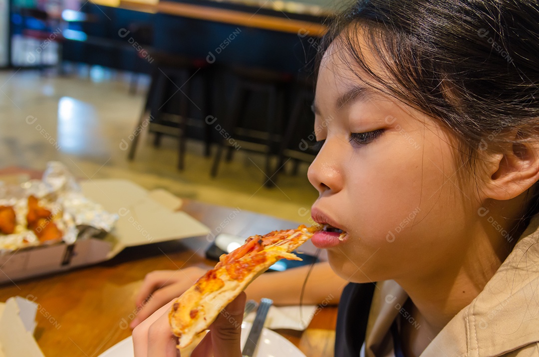 Lindo menino asiático comendo pizza no restaurante.