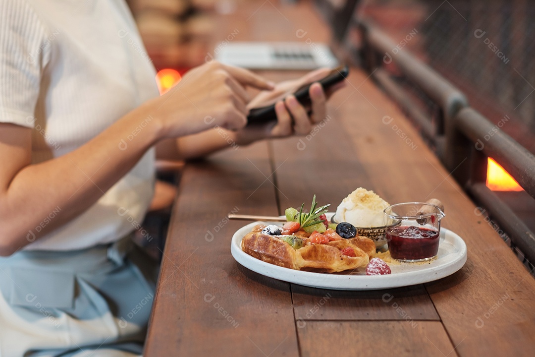 Mulher usando smartphone e comendo sobremesa com frutas e frutas frescas no café