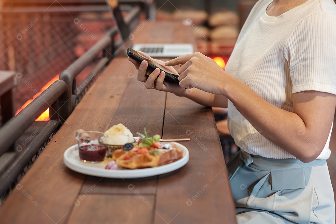 Mulher usando smartphone e comendo sobremesa com frutas e frutas frescas no café