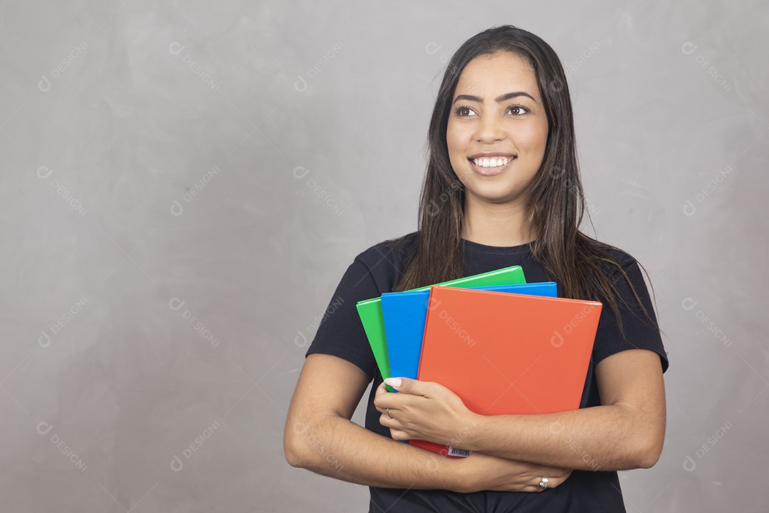 Linda mulher sorridente sobre fundo cinza segurando material escolar