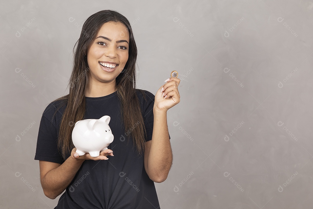 Mulher jovem de camisa preta segurando um cofrinho símbolo de poupança