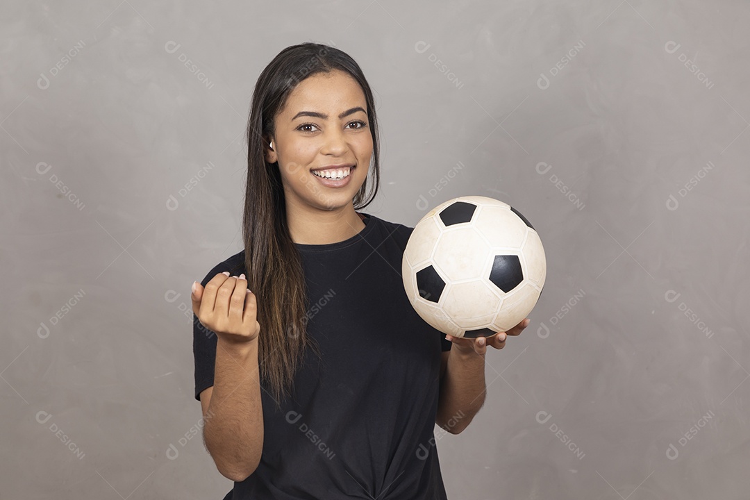 Mulher jovem de camisa preta segurando uma bola de futebol