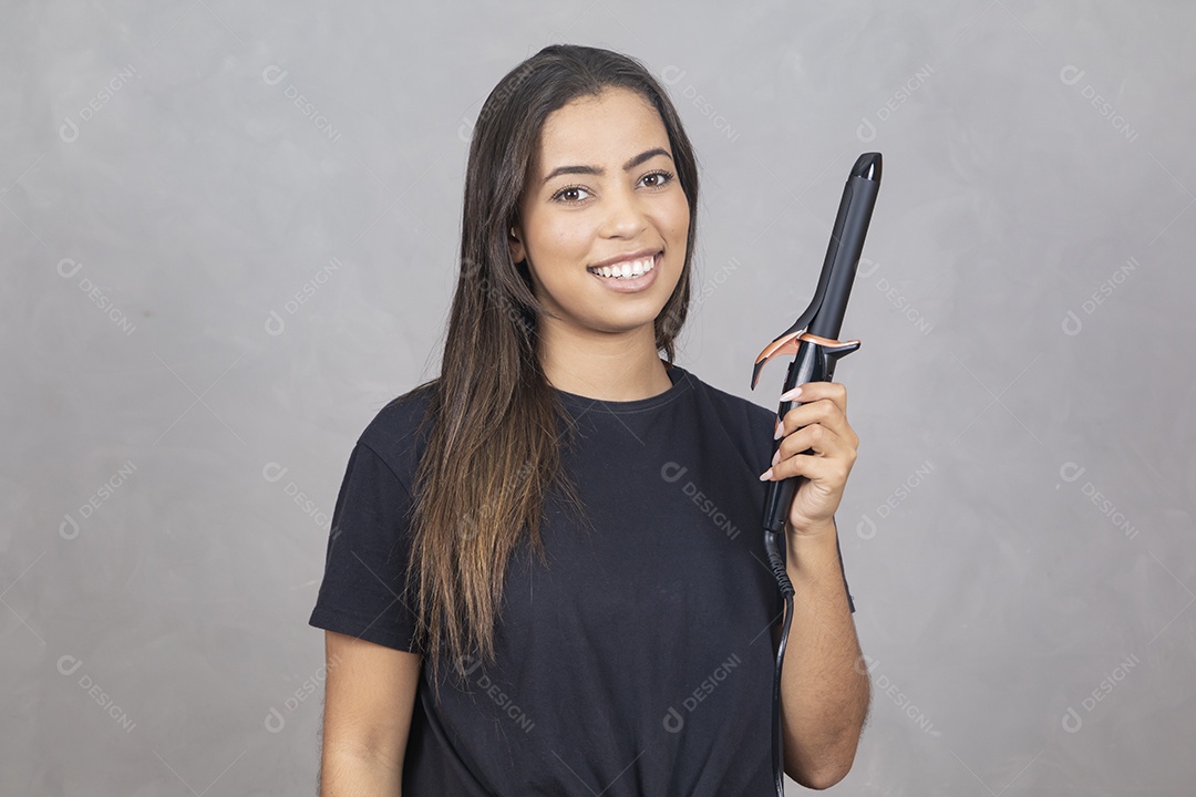 Mulher jovem de camisa preta fazendo gestos e segurando um babyliss
