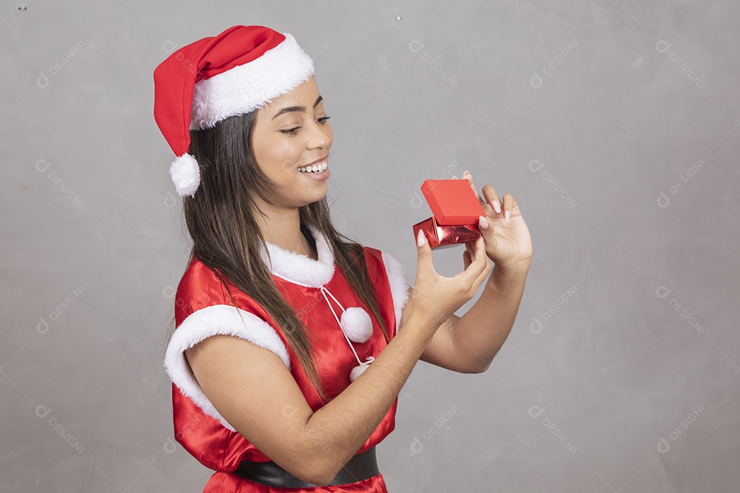 Mulher jovem vestida de Papai Noel segurando uma caixinha pequena de presente