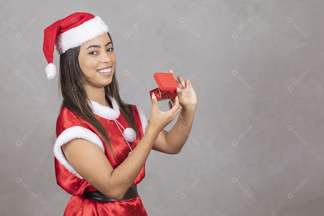 Mulher jovem vestida de Papai Noel segurando uma caixinha pequena de presente