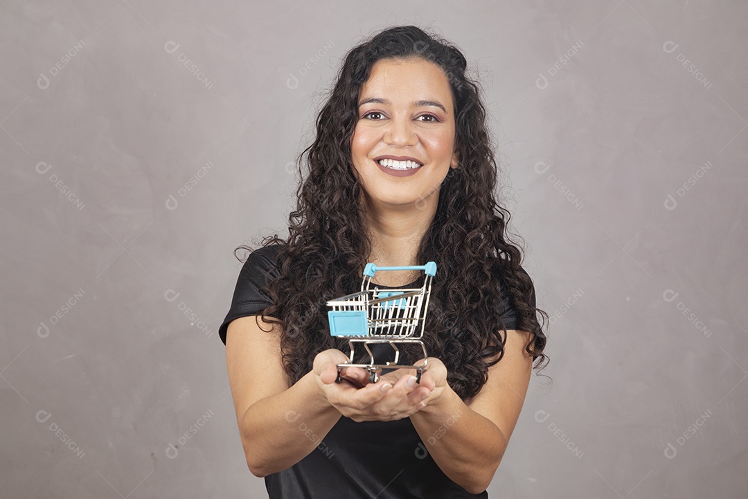 Linda mulher jovem garota sorridente segurando carrinho de compras sobre fundo isolado cinza