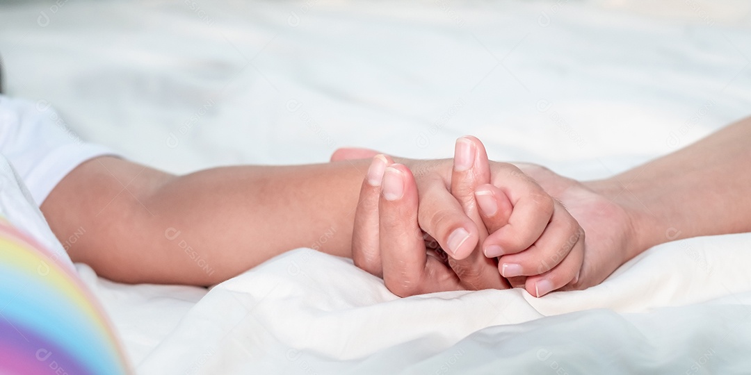 Feche a mãe segurando a mão do bebê na cama branca, ligação de amor