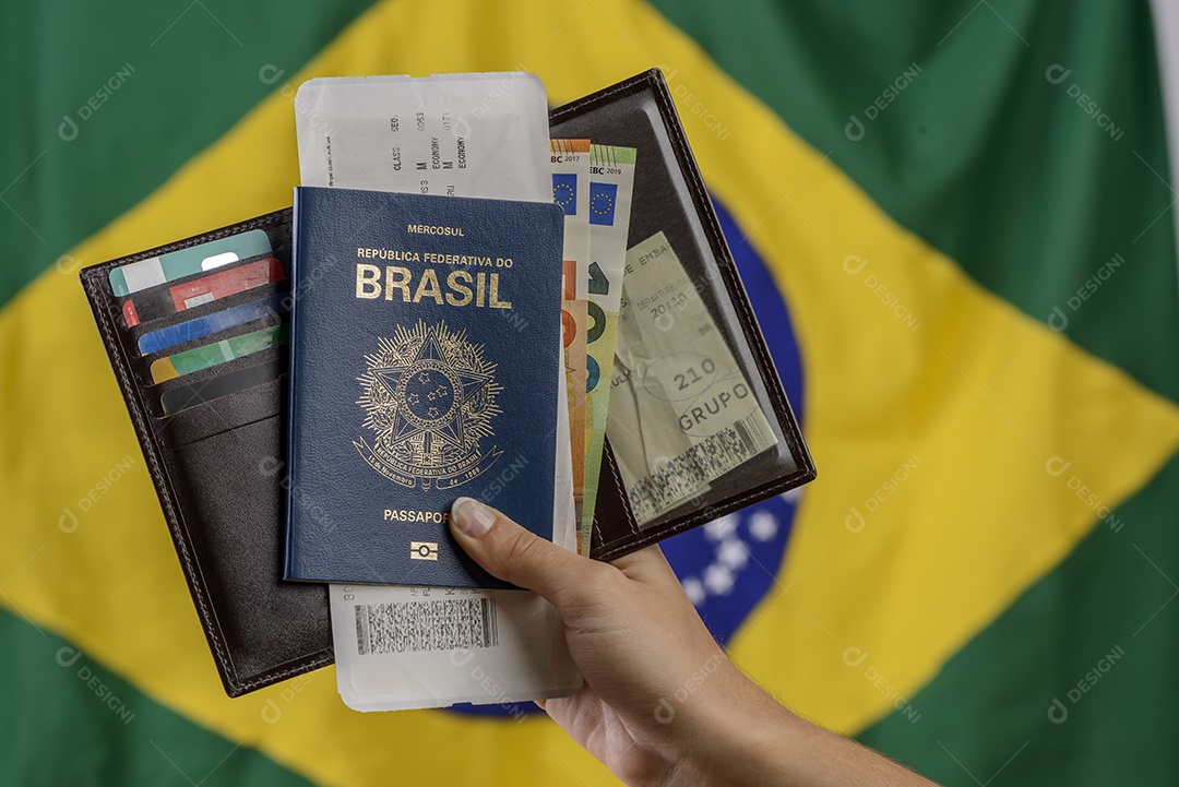 Mão segurando passaporte brasileiro com bandeira brasileira no fundo desfocado.