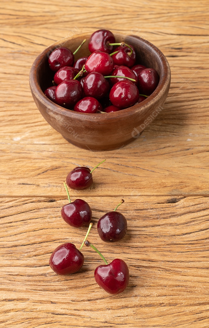Cerejas vermelhas em uma tigela sobre a mesa de madeira.