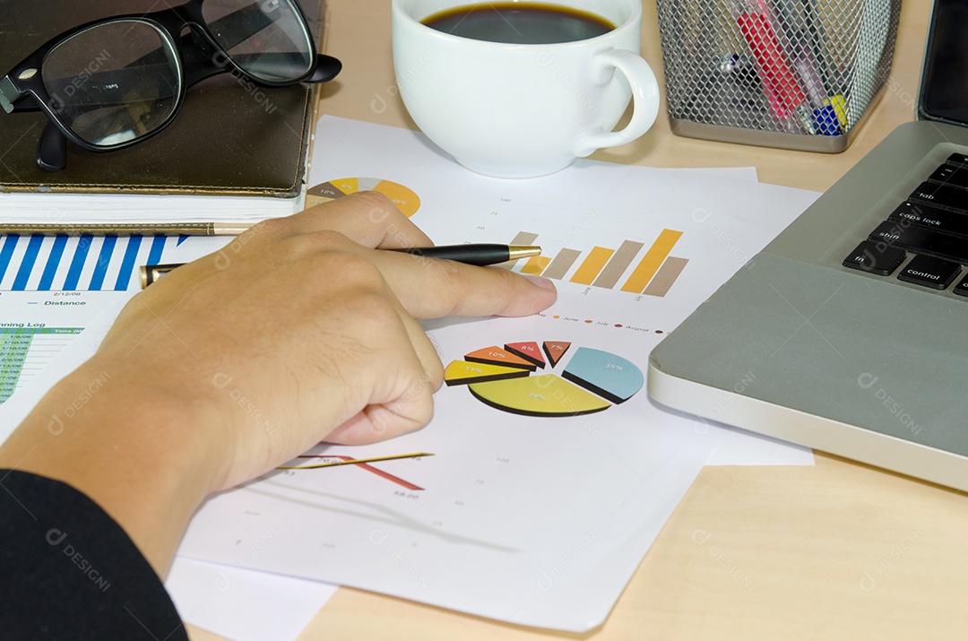 Documentos de negócios analisando gráficos de investimento com laptop.