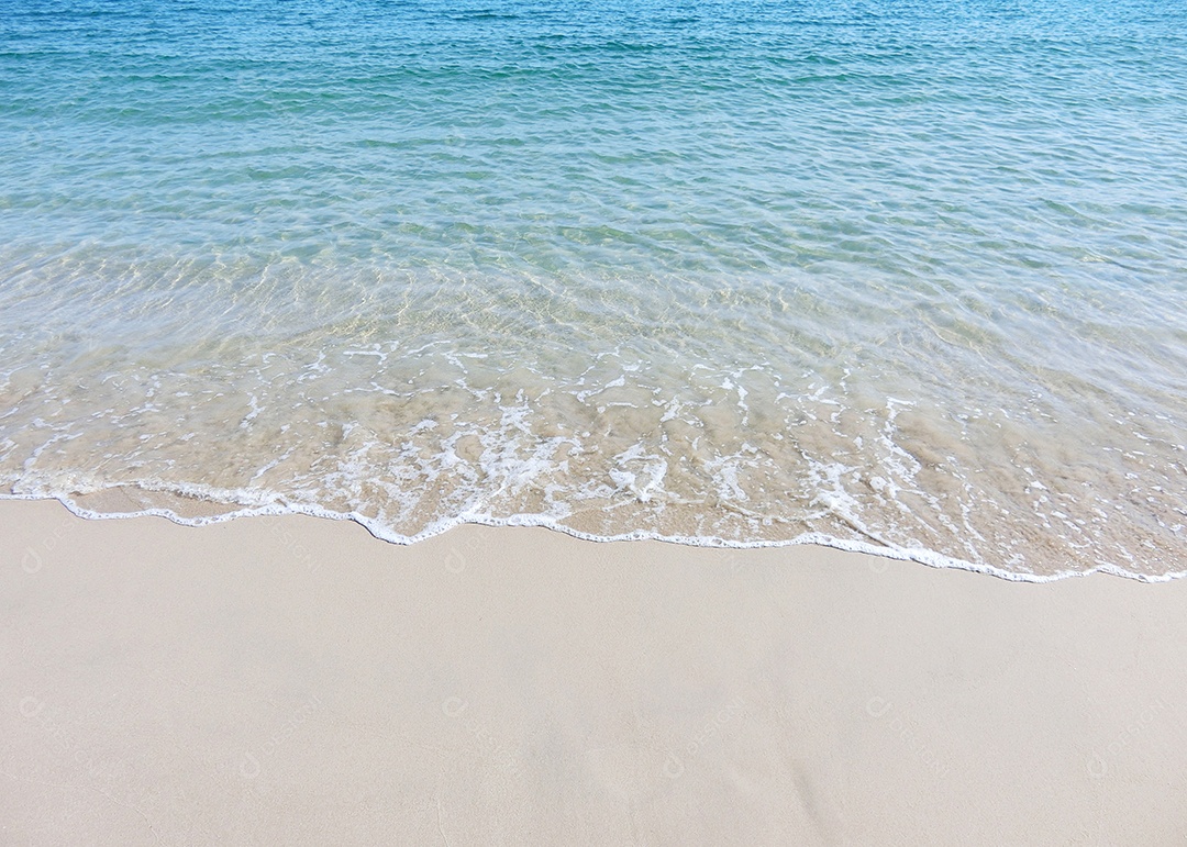 Ondas espumosas em uma praia de areia com água azul do mar em uma praia tropical