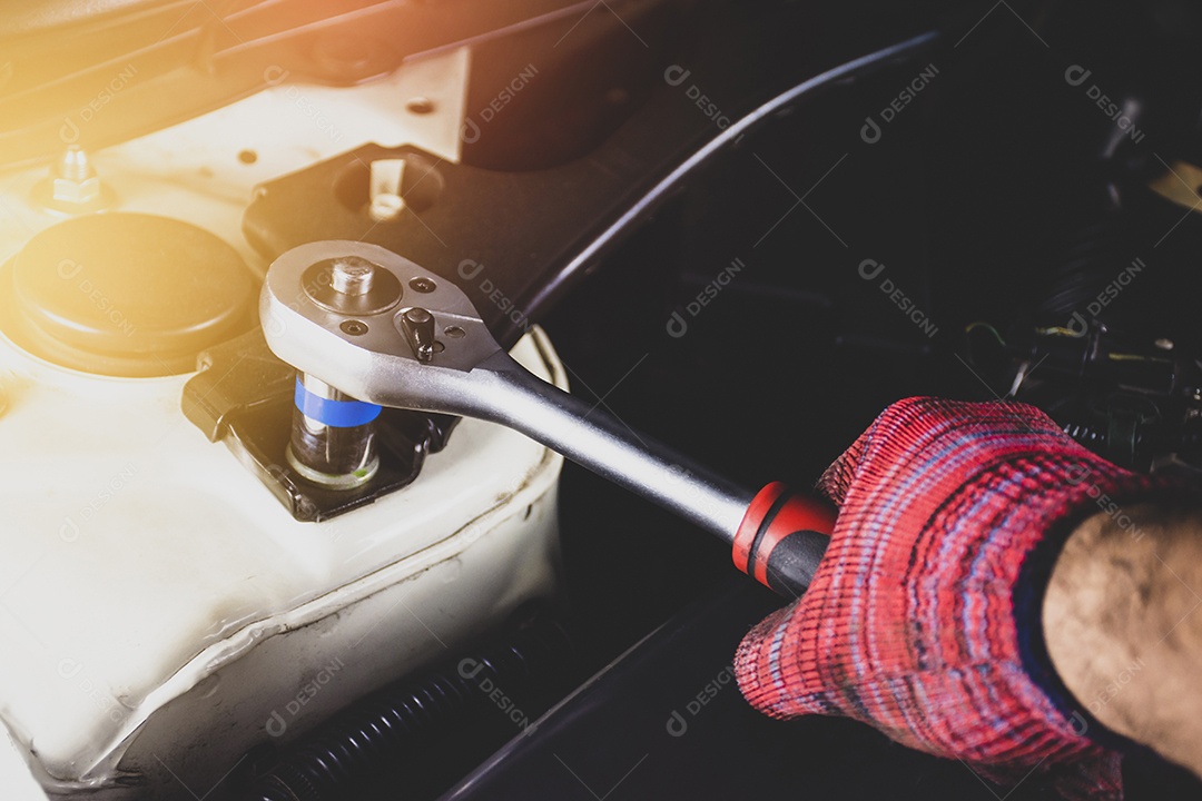 Mão de homem mecânico com luva vermelha usando chave de soquete para reparar o motor de um carro na garagem de reparação de veículos, conceito de reparo automotivo