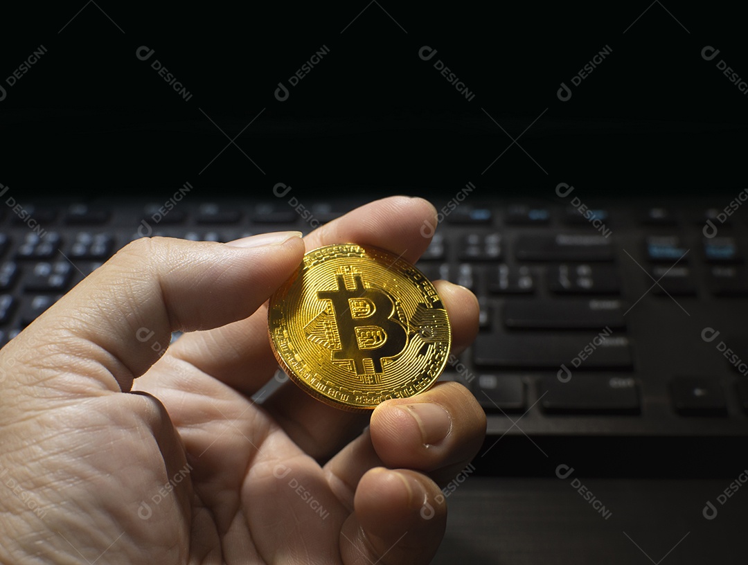 Golden bitcoin segurando em uma mão com o teclado do computador azul