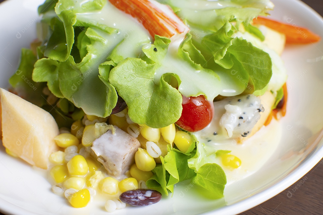 Salada com frutas e legumes frescos cobertos com molho de salada em um prato branco sobre uma mesa de madeira
