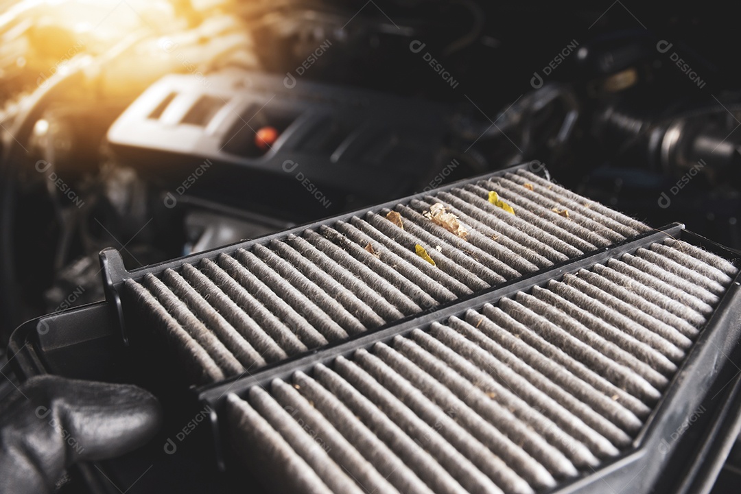 O filtro de ar do carro está sujo em uma mão com o pano de fundo desfocado do motor