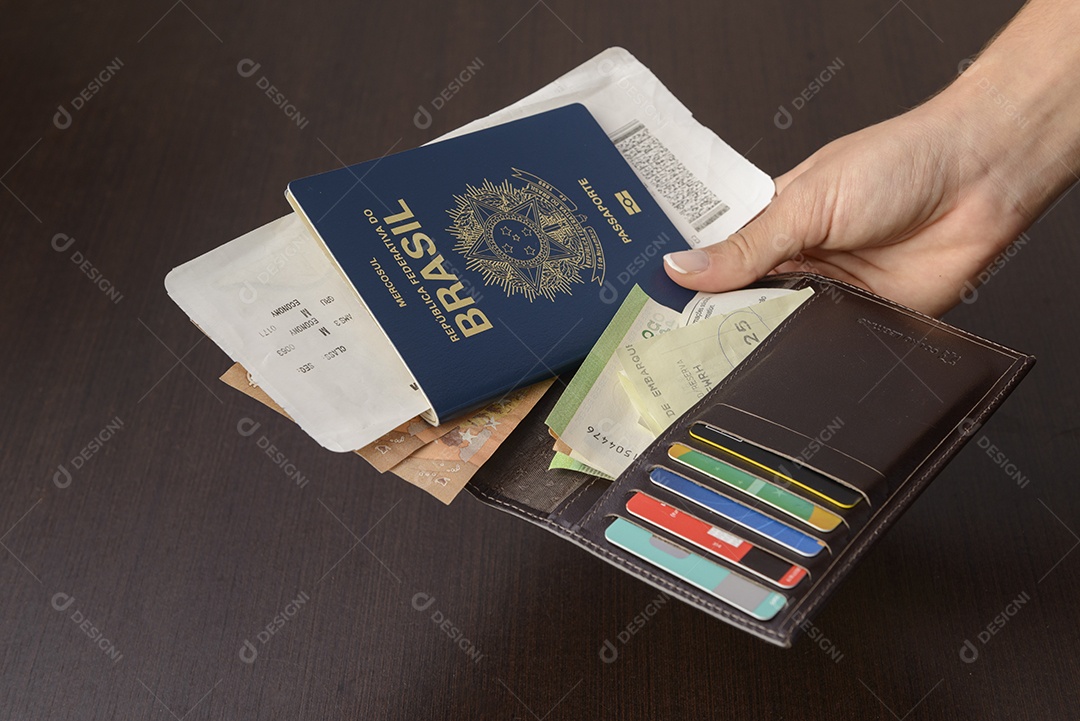 Mão segurando o passaporte brasileiro sobre a mesa.