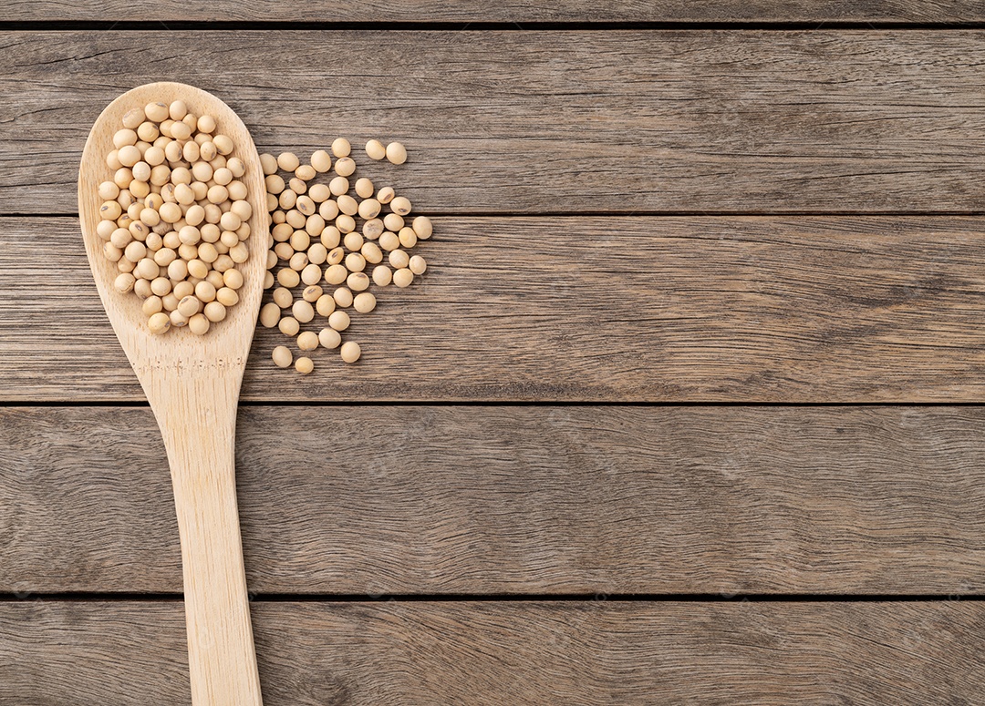 Grãos de soja crus em uma colher sobre mesa de madeira com espaço de cópia.