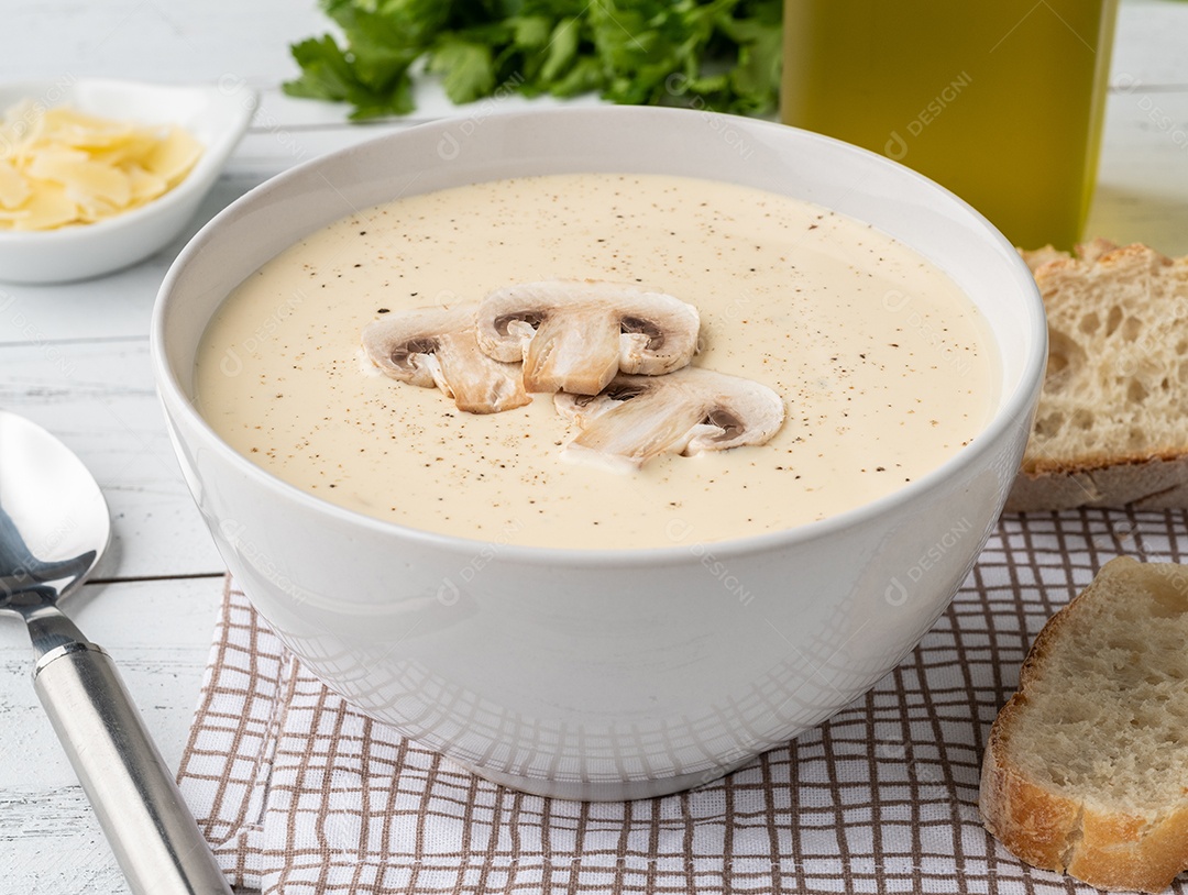 Sopa de cogumelos em uma tigela com fatias de pão e temperos sobre a mesa de madeira.