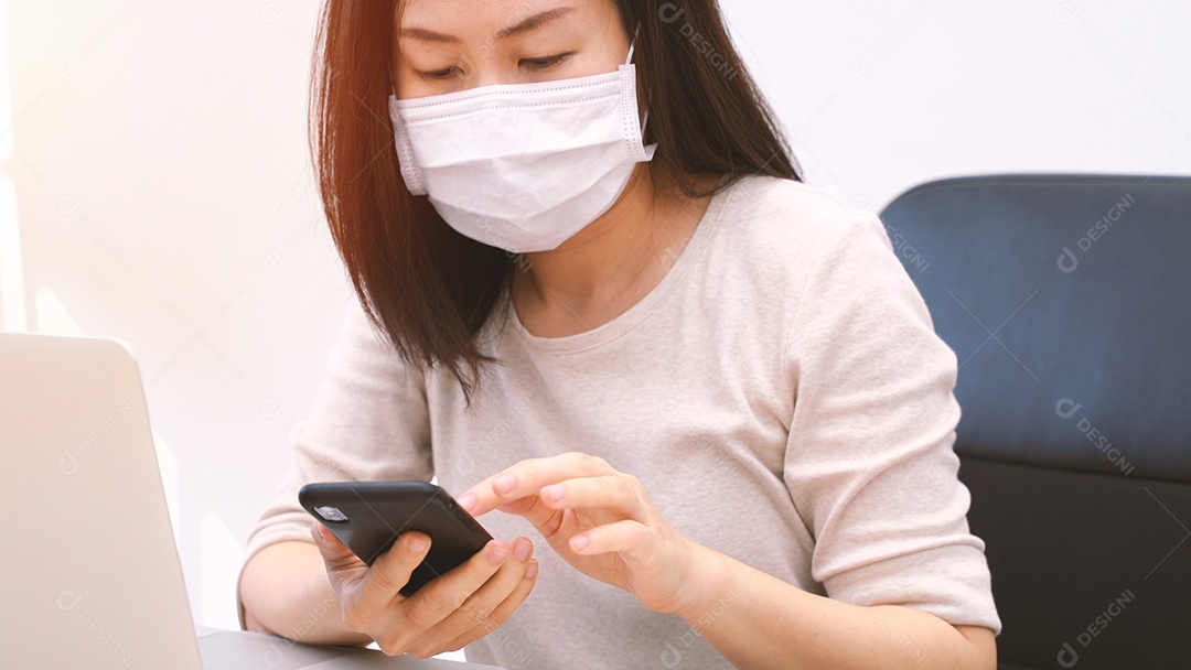 Jovem mulher asiática usando máscara higiênica usando smartphone e trabalho
