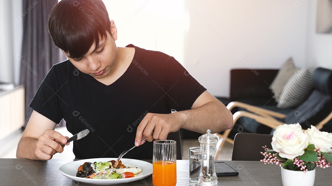 Homem jovem de raça mista asiática comendo café da manhã saudável e bebendo