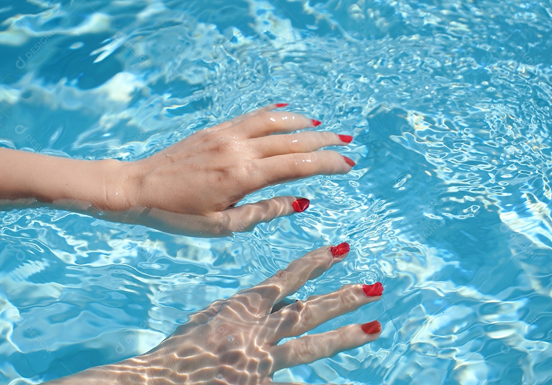 Close-up das mãos da mulher com manicure em vermelho sob piscina clara