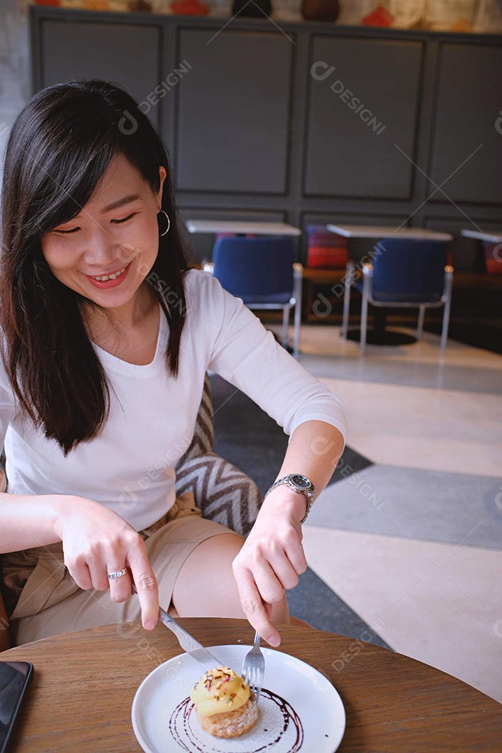 Jovem mulher atraente asiática comendo cupcake doce no café