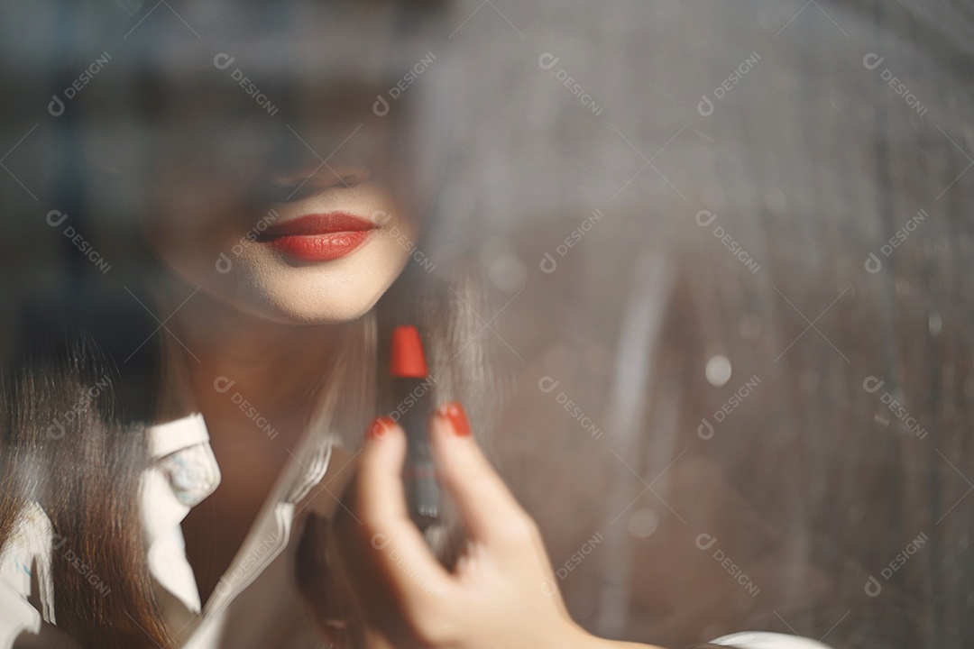 Jovem atraente asiática aplicando maquiagem de batom vermelho