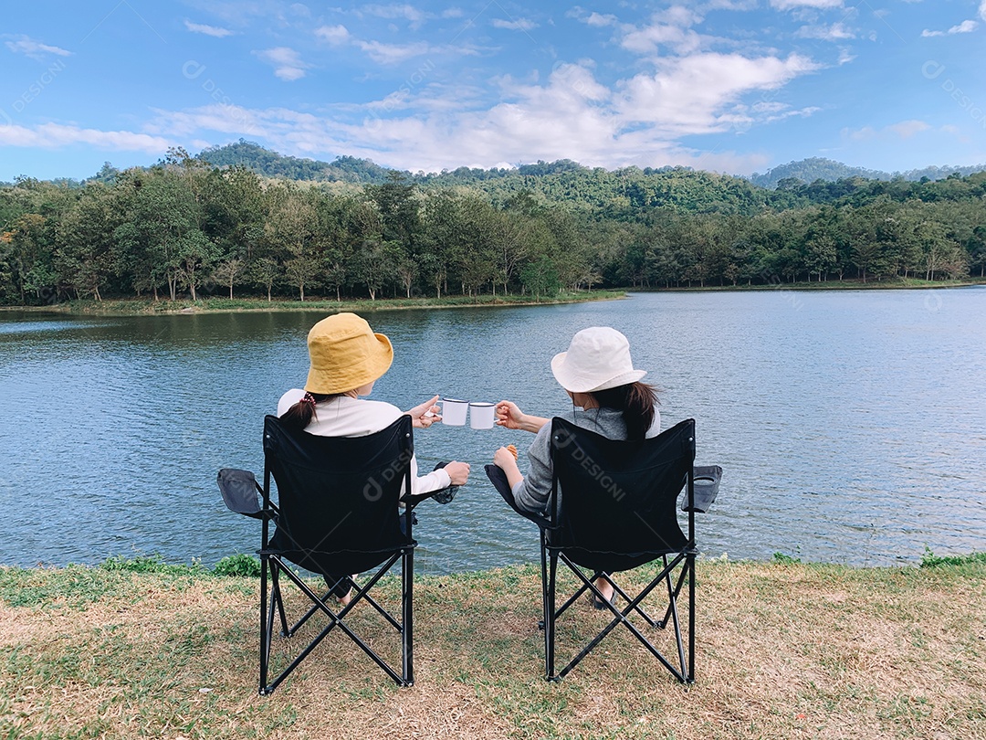 Duas amigas bebendo café e sentadas no acampamento
