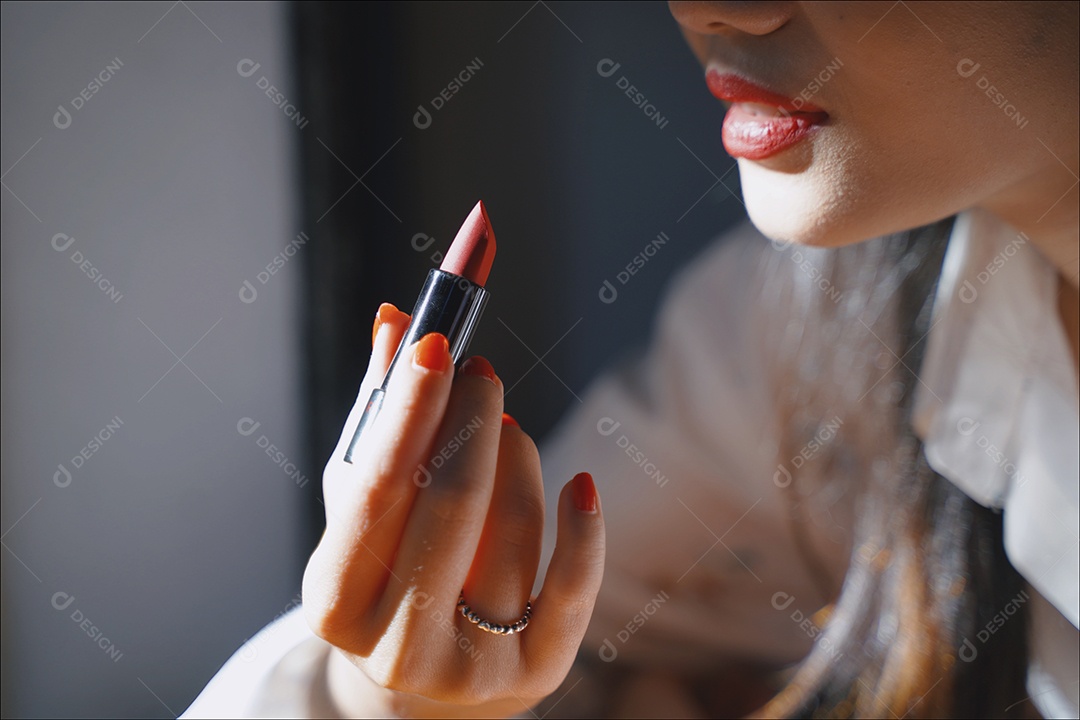 Jovem atraente asiática aplicando maquiagem de batom vermelho