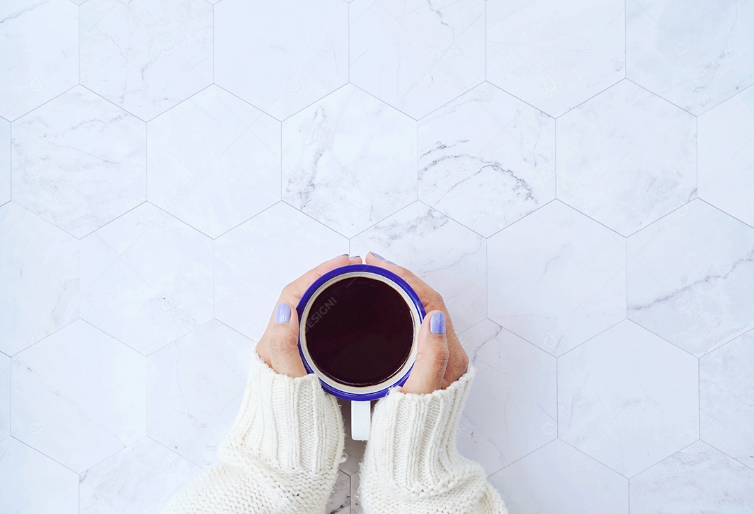 Vista superior das mãos da mulher segurando uma xícara de café quente no mármore branco